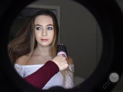 In this Feb. 28, 2018 photo, Matty Nev Luby, standing in front of a ring light, has her hair brushed by her mother Kerrylynn Mahoney in Wethersfield, Conn. Teens and young adults say cyberbullying is a serious problem for people their age, but most don’t think they’ll be the ones targeted for digital abuse. The high school gymnast’s popularity on the lip-syncing app Musical.ly, which merged this summer into the Chinese video-sharing app TikTok, helped win her some modeling contracts. Luby said she's learned