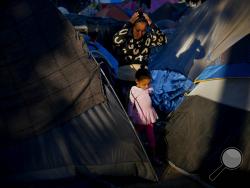 A woman and a girl who traveled a caravan of migrants walks between tents at the Benito Juarez Sports Center which is serving as a shelter in Tijuana, Mexico, Monday, Nov. 26, 2018. The mayor of Tijuana has declared a humanitarian crisis in his border city and says that he has asked the United Nations for aid to deal with thousands of Central American migrants who have arrived. (AP Photo/Ramon Espinosa)