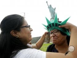 Karen Mejia, left, fits her mother Leonor Chipayo, with a souvenir Statue of Liberty foam visor while visiting the Statue of Liberty, Wednesday, Aug. 14, 2019, in New York. Both women are from Lima, Peru. Long before a Trump administration official suggested the poem inscribed on the Statue of Liberty welcomed only people from Europe, the words captured America's promise to newcomers at a time when the nation was also seeking to exclude many immigrants from landing on its shores. (AP Photo/Kathy Willens)