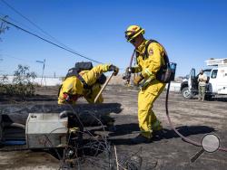 Firefighters with Cal Fire examine a burned down low voltage power pole during the Tick Fire, Thursday, Oct. 25, 2019, in Santa Clarita, Calif. An estimated 50,000 people were under evacuation orders in the Santa Clarita area north of Los Angeles as hot, dry Santa Ana winds howling at up to 50 mph (80 kph) drove the flames into neighborhoods (AP Photo/ Christian Monterrosa)