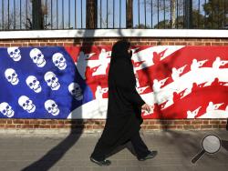 A mourner walk back from a funeral ceremony for Iranian Gen. Qassem Soleimani and his comrades, who were killed in Iraq in a U.S. drone attack on Friday, passing graffiti on the wall of the former U.S. Embassy in Tehran, Iran, Monday, Jan. 6, 2020. A push led by pro-Iran factions to oust U.S. troops from Iraq is gaining momentum, bolstered by a Parliament vote in favor of a bill calling on the the government to remove them. But the path forward is unclear. (AP Photo/Vahid Salemi)