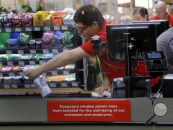 FILE - In this March 26, 2020, file photo, Garrett Ward sprays disinfectant on a conveyor belt between checking out shoppers behind a plexiglass panel at a Hy-Vee grocery store in Overland Park, Kan. From South Africa to Italy to the U.S., grocery workers — many in low-wage jobs — are manning the front lines amid worldwide lockdowns, their work deemed essential to keep food and critical goods flowing. (AP Photo/Charlie Riedel, File)