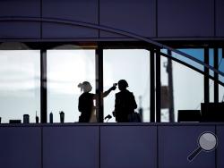 Amid coronavirus concerns, a healthcare worker takes the temperature of a visitor to Essentia Health who was crossing over a skywalk bridge from the adjoining parking deck, Friday, April 10, 2020, in Duluth, Minn. (Alex Kormann/Star Tribune via AP)