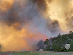 In this image made from video taken May 6, 2020 by the Florida Department of Agriculture and Consumer Services, fire and smoke rise from trees alongside a road in Santa Rosa County, Florida. Wildfires raging in the Florida Panhandle have forced nearly 500 people to evacuate from their homes, authorities said. (Florida Department of Agriculture and Consumer Services via AP)