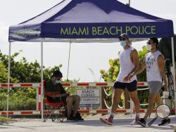 People wearing protective face masks walk past a closed entrance to the beach during the new coronavirus pandemic, Friday, July 3, 2020, in the South Beach neighborhood of Miami Beach, Fla. Beaches throughout South Florida are closed for the busy Fourth of July weekend to avoid further spread of the new coronavirus. (AP Photo/Lynne Sladky)