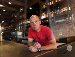 Jeff Brightwell, owner of Dot's Hop House, is framed between protective shielding placed over the bar as he poses for a photo at his establishment in the Deep Ellum entertainment district in Dallas, Thursday, Aug. 20, 2020. (AP Photo/Tony Gutierrez)