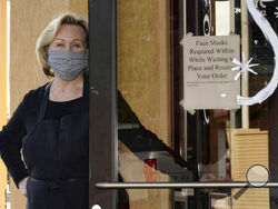 Brenda Luntey, poses for a photo by a sign advising customers to wear face masks that is posted on the door of the San Francisco Deli in Redding, Calif., Thursday, Dec. 3, 2020. Luntey, who owns the deli with her husband, who says she comes from a law enforcement family and is not a rule breaker, is openly violating the state's order to close her restaurant to indoor dining. "I want people to understand we are not thumbing our nose at the government,"said Luntey, "I'm trying to keep my business alive. (AP P
