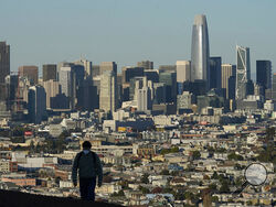FILE - In this Dec. 7, 2020, file photo, a person wearing a protective mask walks in front of the skyline on Bernal Heights Hill during the coronavirus pandemic in San Francisco. California's population has declined for the first time in its history. State officials announced Friday, May 7, 2021, that the nation's most populous state lost 182,083 people in 2020. California's population is now just under 39.5 million. (AP Photo/Jeff Chiu, File)