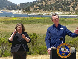 Gov. Gavin Newsom and interpreter Julia Townsend stand at the edge of a diminished Lopez Lake near Arroyo Grande, Calif., Thursday, July 8, 2021. Newsom has asked people and businesses in the nation's most populous state to voluntarily cut how much water they use by 15% amid a drought. Newsom's request is not an order. But it demonstrates the growing challenges of a drought that will only worsen throughout the summer and fall and is tied to recent heat waves. (David Middlecamp/The Tribune (of San Luis Obisp