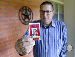 Lance Lowry, a recently retired corrections officer with the Texas State Penitentiary, holds his ID badge on the front porch of his home, Oct. 27, 2021, in Huntsville, Texas. Lowry, an officer for 20 years, became disheartened watching friends and coworkers die from COVID-19, along with dwindling support from his superiors. He left the prison system this summer for a job in long-haul trucking. (AP Photo/Michael Wyke)
