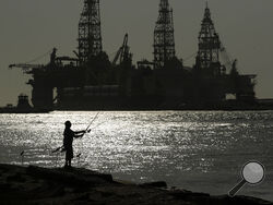 FILE - A man wears a face mark as he fishes near docked oil drilling platforms, Friday, May 8, 2020, in Port Aransas, Texas. The U.S. Interior Department on Wednesday, Nov. 17, 2021, is auctioning vast oil reserves in the Gulf of Mexico estimated to hold up to 1.1 billion barrels of crude. It's the first such sale under President Joe Biden and underscores the challenges he faces to reach climate goals that rely on cuts in fossil fuel emissions. (AP Photo/Eric Gay, File)