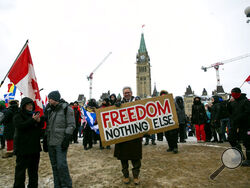 Don Stephens, 65, a retired graphic designer, holds a sign on Parliament Hill to support trucks lined up in protest of COVID-19 vaccine mandates and restrictions in Ottawa, Ontario, on Saturday, Feb. 12, 2022. Stephens said he’s come into Ottawa twice to show support for protesters there. He views them as representatives of a “silent majority that had been longing to have their voice heard.” (AP Photo/Ted Shaffrey)