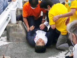 In this image from a video, Japan’s former Prime Minister Shinzo Abe, center, is attended on the ground in Nara, western Japan Friday, July 8, 2022. Abe was shot and critically wounded during a campaign speech Friday. He was airlifted to a hospital but officials said he was not breathing and his heart had stopped. (Kyodo News via AP)