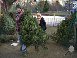 Larry Gurnee carries a $55 Christmas tree he selected with his wife, , Libby Gurnee, background, at a Rotary Club tree sale, Wednesday, Dec. 14, 2022, in South Portland, Maine. Inflation has Americans cutting back on spending in some areas this holiday season but Christmas trees is not one of them, according to the National Christmas Tree Association. (AP Photo/Robert F. Bukaty)