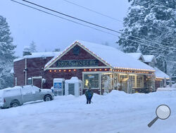 A person shovels snow outside Rome Grocery northeast of Bellingham, Wash., on Tuesday morning, Dec. 20, 2022. Heavy snow, freezing rain and sleet have disrupted travel across the Pacific Northwest, causing widespread flight cancellations and creating hazardous driving conditions. (AP Photo/Lisa Baumann)