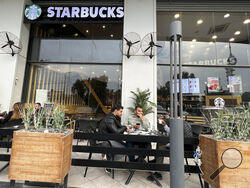 People sit in an unlicensed Starbucks cafe in Baghdad, Iraq, Wednesday, Dec. 21, 2022. Real Starbucks merchandise is imported from neighboring countries to stock the three cafes in the city, but all are unlicensed. Starbucks filed a lawsuit in an attempt to shut down the trademark violation but the case was shuttered after the owner allegedly threatened lawyers hired by the coffee house. (AP Photo/Ali Abdul Hassan)