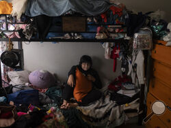 Deneffy Sánchez, 15, rests on a bed he shares with his mother and little sister just feet away from their roommate's bed in Los Angeles, Saturday, Sept. 9, 2023. In Los Angeles, housing insecurity is one of the biggest reasons kids have missed school since the pandemic and struggle to catch up. (AP Photo/Jae C. Hong)