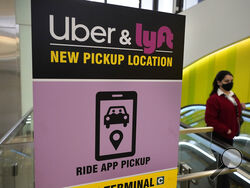 FILE - A passerby walks past a sign offering directions to an Uber and Lyft ride pickup location at an airport, Feb. 9, 2021, in Boston. Drivers for Uber and Lyft will earn a minimum pay standard of $32.50 per hour under a settlement announced, Thursday, June 27, 2024, by Massachusetts Attorney General Andrea Campbell, a deal that also includes a suite of benefits and protections. (AP Photo/Steven Senne, File)