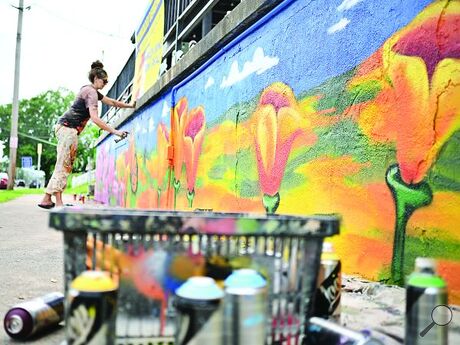 Jules Muck, who paints under the name Muck Rock, from Venice, California spray paints flowers on a wall of the Intoxicology Department bar in Berwick on Tuesday as part of her tour around the country.