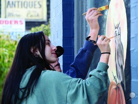 Drew Mumich/ Press Enterprise Columbia County Christian School Juniors Camille Cunningham, 15 (left) and Lyman Runkle,16 (right) puts the finishing touches on a painting on the front window of Creative Dog, Bloomsburg, on Wednesday.