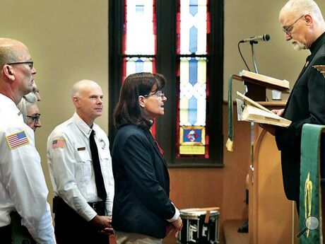 PASTOR GORDON SMITH, right, commissions Pastor Kym Eichelberger, center, as the Valley Chemical Fire Company Chaplain during the company’s 100th anniversary recognition service in Saint Paul Evangelical Lutheran Church in Numidia on Sunday. At left are fire company officers, from left,Chief Mark Sharrow, Kim and Hank Meiss (partly hidden) and Cale Beaver. Eichelberger is the pastor at the Kulp United Methodist Church.