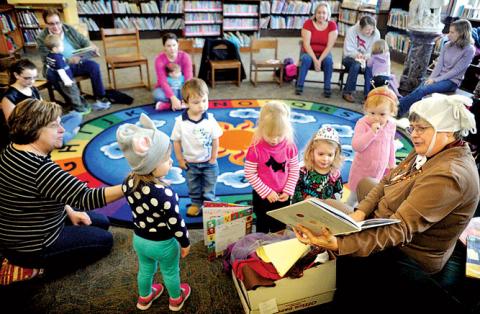 Bloomsburg Public Library children’s librarian Karen Roszel, at right, reads from “Press Here” by Herve Tullet during Toddle Time at the library on Monday morning.