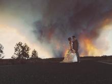 In this Saturday, June 7, 2014 photo provided by Josh Newton, newlyweds Michael Wolber and April Hartley pose for a picture near Bend, Ore., as a wildfire burns in the background. Because of the approaching fire, the minister conducted an abbreviated ceremony and the wedding party was evacuated to a downtown Bend park for the reception. (AP Photo/Josh Newton)