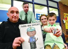 Salem Township student Aiden Lee Foust, 6, holds the newest challenge coin which features an image he colored as he sits on his mother’s, Kathleen Foust along with Salem Police Chief Michael McNeal, left, and Salem Elementary principal Patrick Sharkey Monday afternoon at the school. 