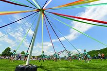 Colored ribbons extend like wheel spokes from a pole. Children hold the ends of the ribbons.