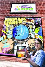 Bloomsburg Children’s Museum director Ginny Weibel stands by the museum’s augmented reality mural in the Miller Ave. Pocket Park, just off Main Street in downtown Bloomsburg on Thursday. She is holding an iPad connected to the mural displaying the solar system. 