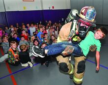 Washington Fire and Hose Company Lt. Colby Kressler carries second grader Kade Broadt through the middle of students in the gym at the Danville Primary School Thursday morning while demonstrating a rescue from a fire. The fire companies from Danville and Mahoning Township have been visiting the schools this week with fire prevention week. 