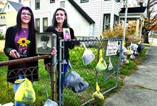 Press Enterprise/Bill Hughes Amy Bacon, left, and her daughter Christine Bacon, hold photos of Amy’s late mother, Evelyn Rankin, while standing in Bloomsburg along a West Fifth Street fence on family property on Sunday morning. Carrying on a tradition started by Rankin, the women are hanging winter clothing in weather-protecting plastic bags, free for the taking. The bags are marked with a size and a short description of the article inside. 