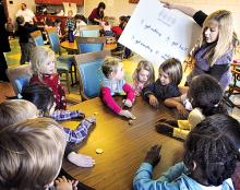 Preschool teacher Shelly Emery holds a chart with dreidel game rule while her students take turns spinning the four-sided top during a Hanukkah celebration at Saint Cyril Academy Preschool and Kindergarten in Danville on Friday,