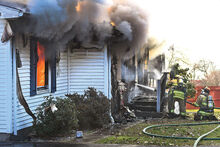 Firefighter pour water into the front door of this home as flames consume a side room Monday morning in Huntington Township.