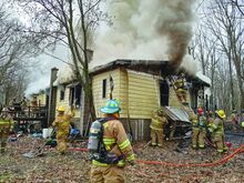 Smoke pours from a yellow house as firefighters work to douse it.