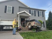 A firefighter takes a photo of an SUV that buried itself in a house early Thursday morning, trapping the homeowners inside. The driver was flown to a hospital.