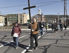 Joel Burley, top photo, carries the cross while leading a Community Good Friday Cross Walk across Bloom Street in Danville Friday morning. The group stopped at seven different churches during the procession.