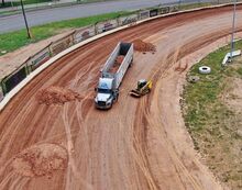 A truck dumps clay on one corner of the Bloomsburg Fair Raceway on Monday morning. A crew is covering the track with a type of clay that creates less dust, fair officials say.