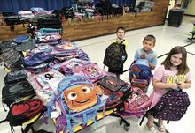 Millville Elementary School students, from left, Jedadaih Shuman, 9; Daniel Leach, 7; and Octavia Nevel, 6, display their new backpacks in the school cafeteria/auditorium Thursday. The school recently received a donation of more than 600 new backpacks and will distribute them to students Monday between 3-6 p.m.