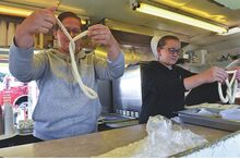 A young woman holds up a twist of dough as her sister prepares to put a raw pretzel on a baking sheet.