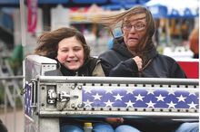 A spinning ride at the Bloomsburg fair has the little boy on the left of the car beaming. The woman sharing the car is grimacing - it looks like she can't wait for the ride to end. 