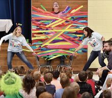 Millville Elementary School Reading Specialists Nevin Iliev, left, and Aimee Diehl pull the chairs from under sixth-grade teacher Blaine Eddy, who students had duct taped to a wall in the school cafeteria Friday morning as a reward for reading 100 hours.