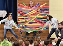 Millville Elementary School Reading Specialists Nevin Iliev, left, and Aimee Diehl pull the chairs from under sixth-grade teacher Blaine Eddy, who students had duct taped to a wall in the school cafeteria Friday morning as a reward for reading 100 hours.